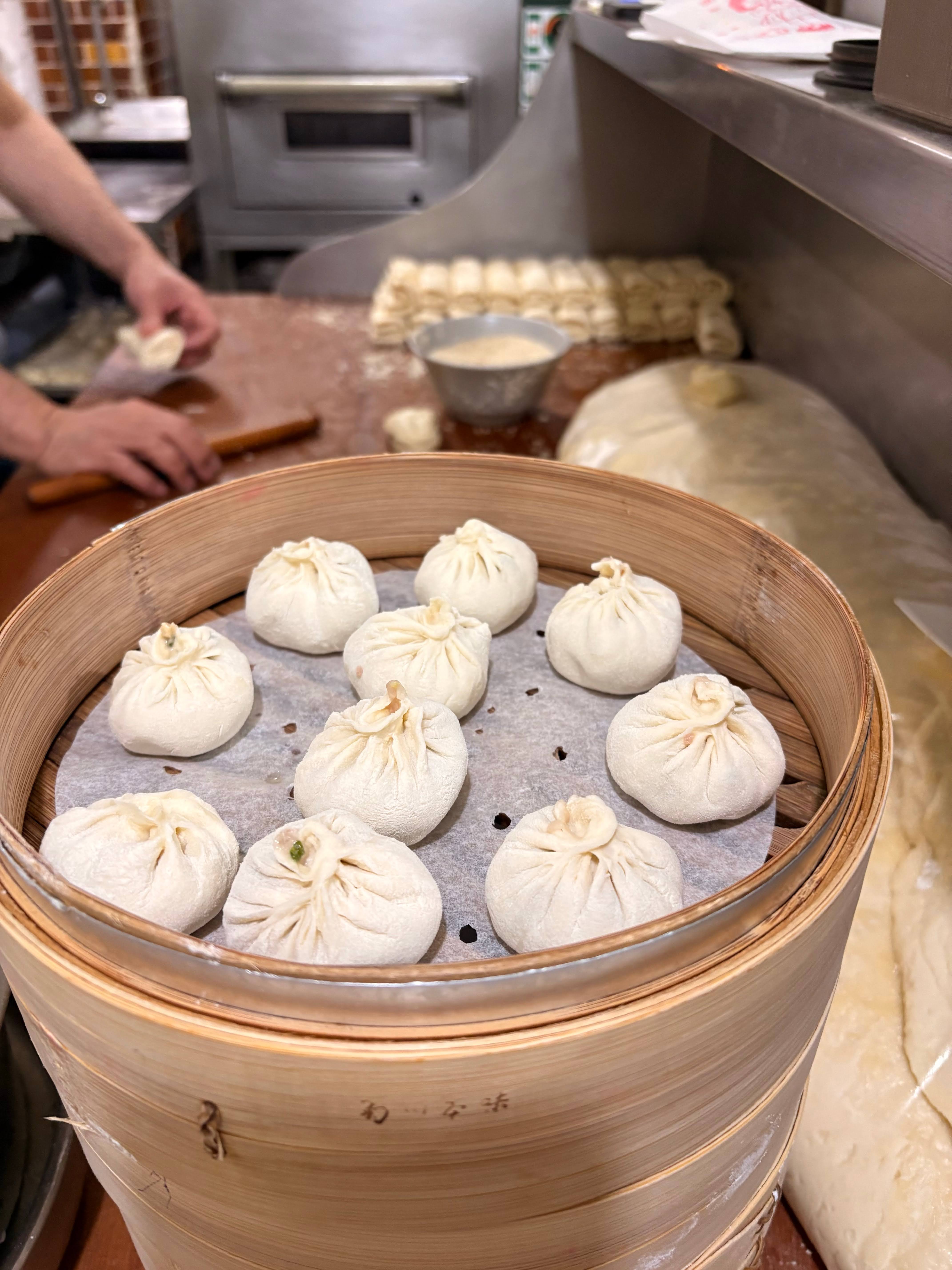 竹製蒸籠中剛蒸好的小籠包，後方師傅正在包製內餡